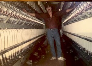 A coloured photograph of a British Asian man stood in John Fosters mill, posing by the machinery. Photograph: Arshad Mahmood