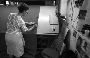 Black and white photograph of a female burler and mender, repairing a piece of cloth at Drummonds Mill. Photograph: Tim Smith