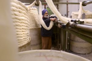 A coloured photograph of a British Asian man carding at Howarth Scouring Company. Photograph: Tim Smith