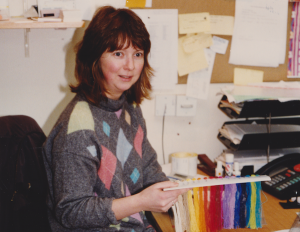 A coloured photograph of a female textile designer sitting at her desk holding colourful thread samples. Photograph: Richard Smith